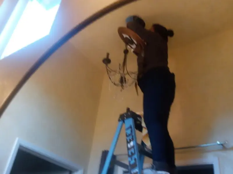 Electrician installing a chandelier in a Raleigh Hills residence